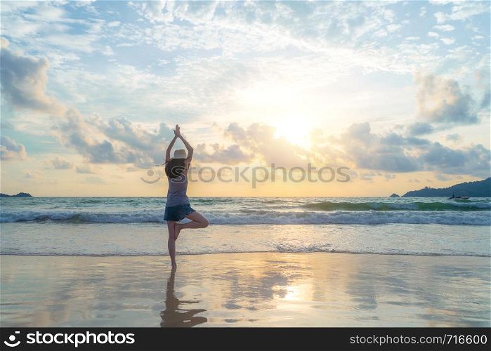 Happy Asian woman practicing yoga or exercising at the beach during travel holidays vacation outdoors at ocean or nature sea at sunset time, Phuket, Thailand