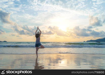 Happy Asian woman practicing yoga or exercising at the beach during travel holidays vacation outdoors at ocean or nature sea at sunset time, Phuket, Thailand