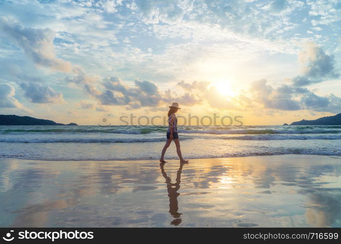 Happy Asian woman relaxing and enjoying at the beach during travel holidays vacation outdoors at ocean or nature sea at sunset time, Phuket, Thailand