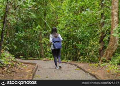 Happy Asian woman relaxing and enjoying at the tropical forest with trees during travel trip and holidays vacation outdoors at national park, Kanchanaburi, Thailand.