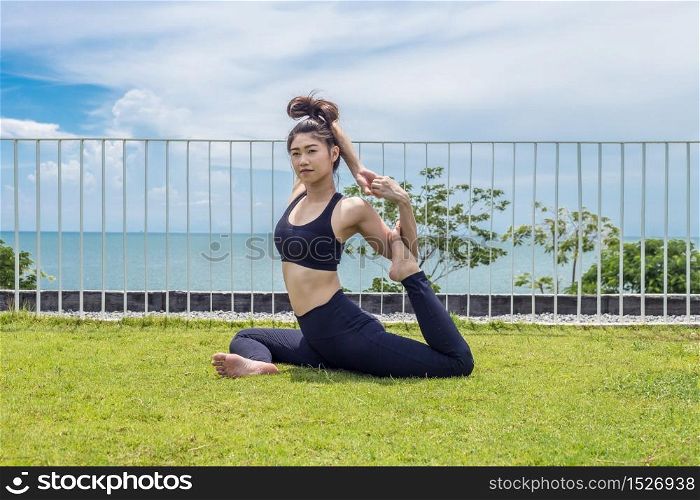 Happy Asian woman relaxing in yoga mermaid pose with beautiful sea view