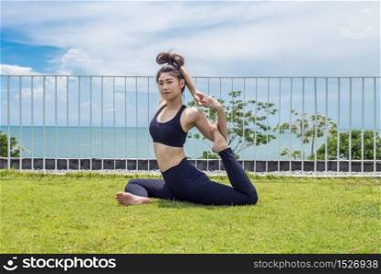 Happy Asian woman relaxing in yoga mermaid pose with beautiful sea view