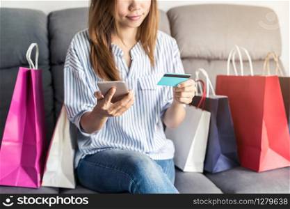 Happy asian woman sitting on sofa and holding credit card and smart phone for shopping online payment and colourful shopping bags, Online shopping concept. Happy asian woman holding credit card and smart phone