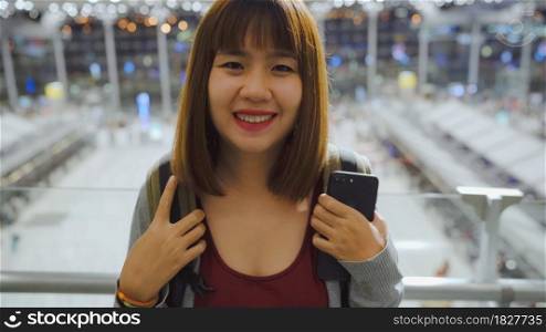 Happy Asian woman smiling to camera while staying at terminal in international airport, female tourist ready to travel on vacation. Lifestyle women happy holiday in the airport concept.