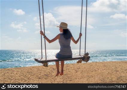 Happy Asian woman swinging on a swing at the beach during travel trip on holidays vacation outdoors at ocean or nature sea at noon, Phuket, Thailand