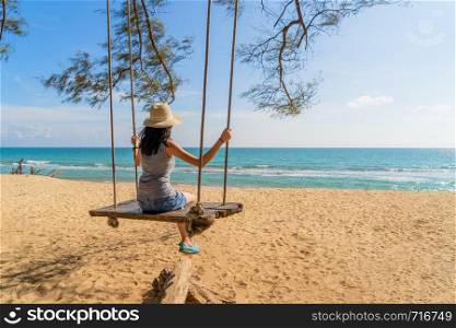Happy Asian woman swinging on a swing at the beach during travel trip on holidays vacation outdoors at ocean or nature sea at noon, Phuket, Thailand