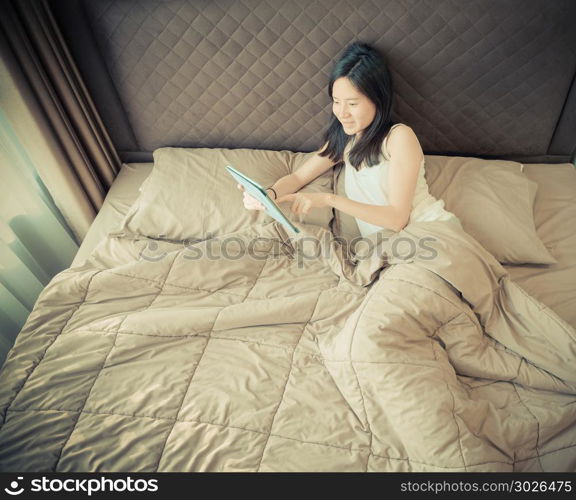 Happy Asian woman using a tablet on bed in bedroom