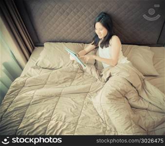 Happy Asian woman using a tablet on bed in bedroom