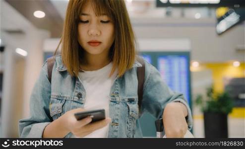 Happy Asian woman using and checking her smartphone in terminal hall while waiting her flight at the departure gate in international airport. Women happy in airport concept.