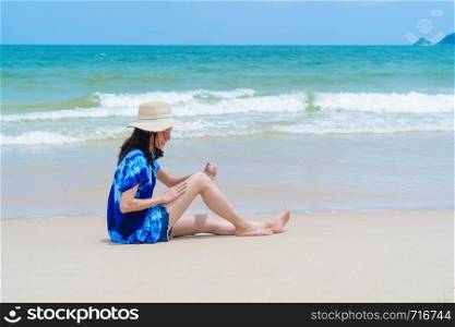 Happy Asian woman wear sunscreen to protect her skin at the beach during travel holidays vacation outdoors at ocean or nature sea at noon, Phuket, Thailand