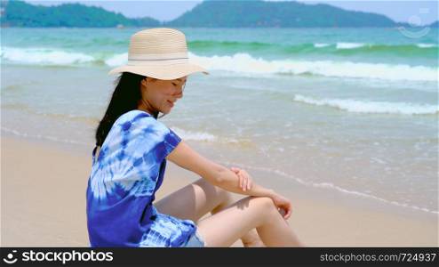 Happy Asian woman wear sunscreen to protect her skin at the beach during travel holidays vacation outdoors at ocean or nature sea at noon, Phuket, Thailand