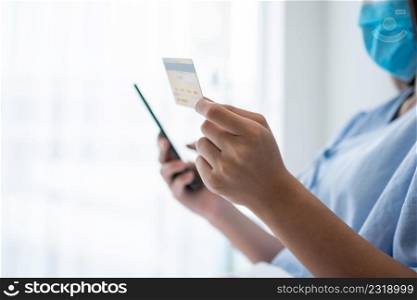Happy Asian woman wearing a medical mask and holding mock up credit /insurance card and smartphone in a hospital bed for Check health insurance eligibility. Insurance policy by bank, payment medical