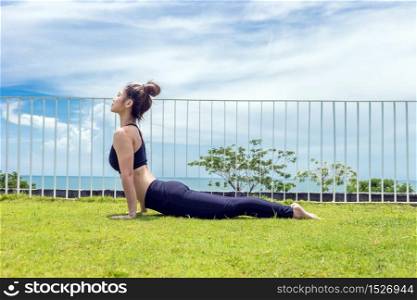Happy Asian woman wearing black sport wear practice yoga Cobra pose with beautiful sea view,Feeling so comfortable and relax in holiday