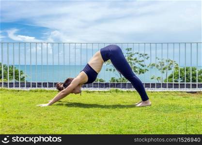 Happy Asian woman wearing black sport wear practice yoga Downward dog pose with beautiful sea view,Feeling relax and comfortable,Healthy Concept