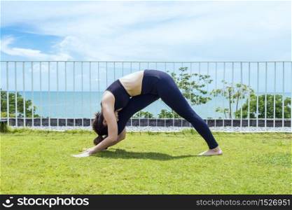 Happy Asian woman wearing black sport wear practice yoga Hamstring Stretching pose with beautiful sea view,Feeling relax and comfortable,Healthy Concept