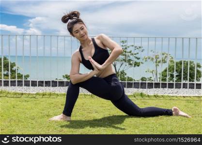 Happy Asian woman wearing black sport wear practice yoga low lunge pose with beautiful sea,Feeling relax and comfortable,Healthy Concept
