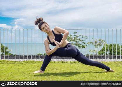 Happy Asian woman wearing black sport wear practice yoga low lunge pose with beautiful sea,Feeling relax and comfortable,Healthy Concept