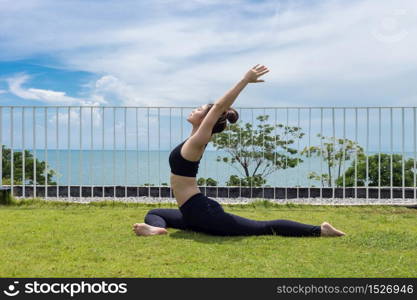 Happy Asian woman wearing black sport wear practice yoga Pigeon pose with beautiful sea view,Feeling relax and comfortable,Healthy Concept