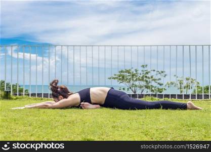 Happy Asian woman wearing black sport wear practice yoga Pigeon pose with beautiful sea view,Feeling relax and comfortable,Healthy Concept