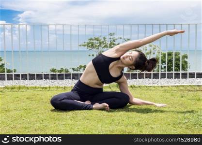 Happy Asian woman wearing black sport wear practice yoga Seated side stretch pose with beautiful sea,Feeling relax and comfortable,Healthy Concept