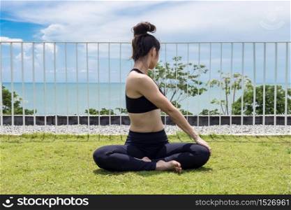 Happy Asian woman wearing black sport wear practice yoga Seated Twist pose with beautiful sea,Feeling relax and comfortable,Healthy Concept