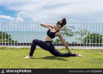 Happy Asian woman wearing black sport wear relaxing in yoga High Lunge twist pose with beautiful sea view,Healthy Concept
