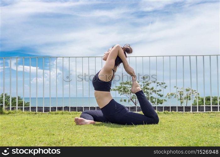 Happy Asian woman wearing black sport wear relaxing in yoga King Pigeon pose with beautiful sea view,Healthy Concept