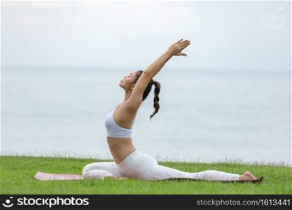 Happy Asian woman wearing white sport wear practice yoga Pigeon pose on the beach with beautiful sea in Tropical island,Feeling comfortable and relax in holiday,Vacations Concept