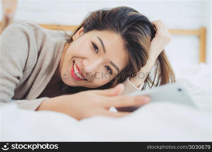Happy Asian women are using smart phone on the bed in morning. A. Happy Asian women are using smart phone on the bed in morning. Asian woman in bed checking social apps with smartphone. Smiling woman surfing net with cellphone at home. Mobile addict concept.