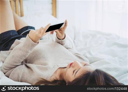Happy Asian women are using smart phone with black blank empty screen on the bed in morning. Asian woman in bed checking social apps with smartphone. Smiling woman surfing net with cellphone at home.