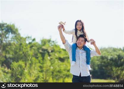 Happy Asian young family father and carrying an excited girl on shoulders having fun and enjoying outdoor lifestyle together playing aircraft toy on sunny summer day, Father’s day concept