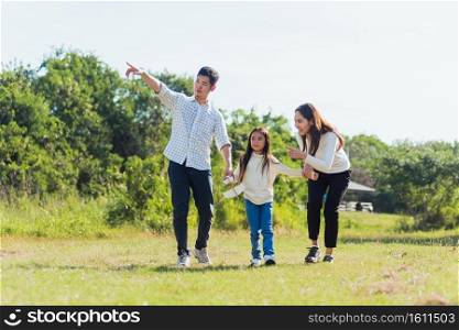 Happy Asian young family father, mother and child little girl having fun and enjoying outdoor walking down the road outside together in green nature park on a sunny summer day