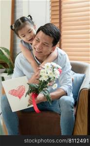 Happy Asian young father getting bunch of flowers and handmade card congratulations on Fathers Day from little cute daughter. Dad is piggyback ride kid with love in living room at home