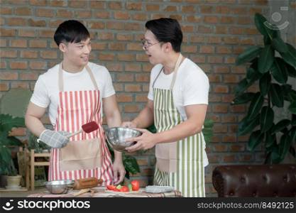 Happy Asian young LGBT gay couple with apron cooking together. Handsome men mixing salad dressing and cutting tomato cucumber in kitchen at home. Relationship of homosexual lifestyle concept