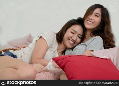 Happy Asian young LGBT women couple hugging smiling and sitting on sofa together in living room at home. LGBT relationship lifestyle concept