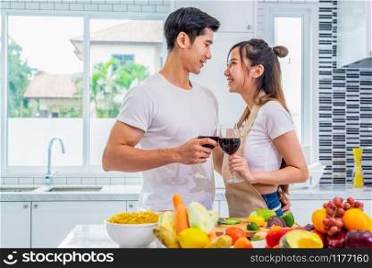 Happy Asian young married couple drinking wine and looking each other in home kitchen. Boyfriend and girlfriend cooking together. People lifestyle and romantic relationship concept. Valentines day
