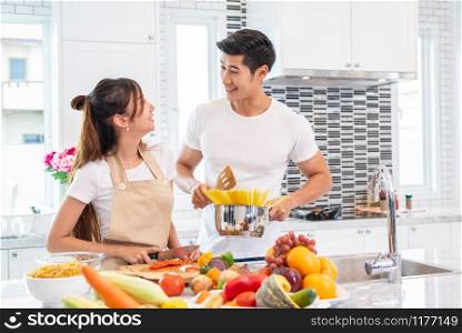 Happy Asian young married couple prepare for making spaghetti bolognese in kitchen. Boyfriend and girlfriend cooking together. People lifestyle and romantic relationship concept. Valentines day indoor