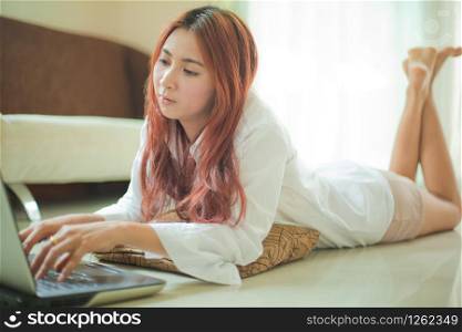 Happy asian young woman lying using laptop at home