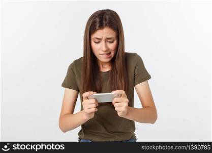 Happy attractive brunette girl joying win in video game on smartphone, isolated over grey background.. Happy attractive brunette girl joying win in video game on smartphone, isolated over grey background