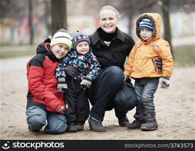 Happy attractive mother with her three young children posing outdoors together in their thick warm winter clothing