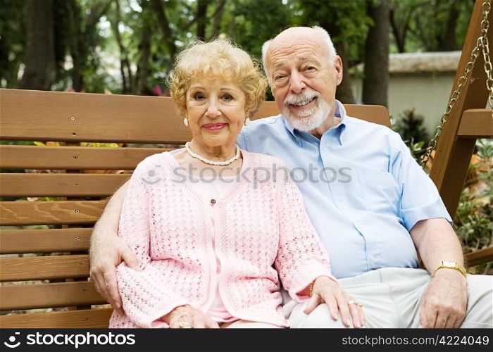 Happy, attractive senior couple relaxing together on a swing in the park.