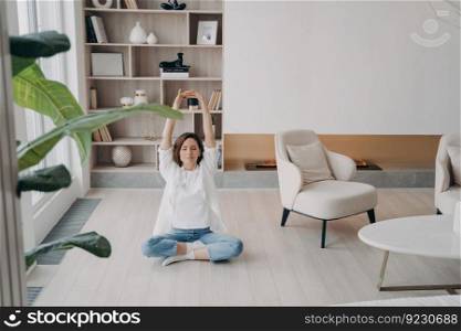 Happy attractive woman is practicing yoga and meditation on floor. European girl is sitting in lotus pose. Morning fitness at home. Mental health, relaxation and stress relief on quarantine.. Happy european woman is practicing yoga sitting in lotus pose. Stress relief on quarantine.