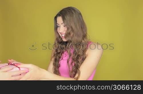 Happy attractive woman with long wavy brunette hair receiving a gift for her birthday on a yellow studio background