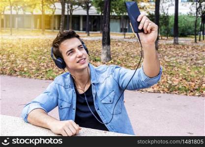 Happy attractive young man in headset taking selfie on his mobile phone. Dressed in jeans shirt