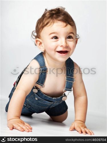 Happy baby boy creeping on studio floor, beautiful cute cheerful kid playing indoor, healthy child expressing joy, toddler having fun, adorable sweet infant close up portrait, little model wears jeans