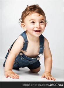 Happy baby boy creeping on studio floor, beautiful cute cheerful kid playing indoor, healthy child expressing joy, toddler having fun, adorable sweet infant close up portrait, little model wears jeans