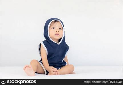Happy baby boy wearing blue hooded sitting on bed, kids playing concept