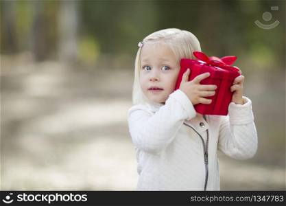 Happy Baby Girl Holding Red Christmas Gift Outdoors.