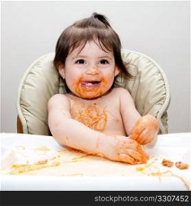 Happy baby having fun eating messy covered in Spaghetti Angel Hair Pasta red marinara tomato sauce.