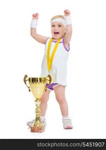 Happy baby in tennis clothes with medal and goblet rejoicing success